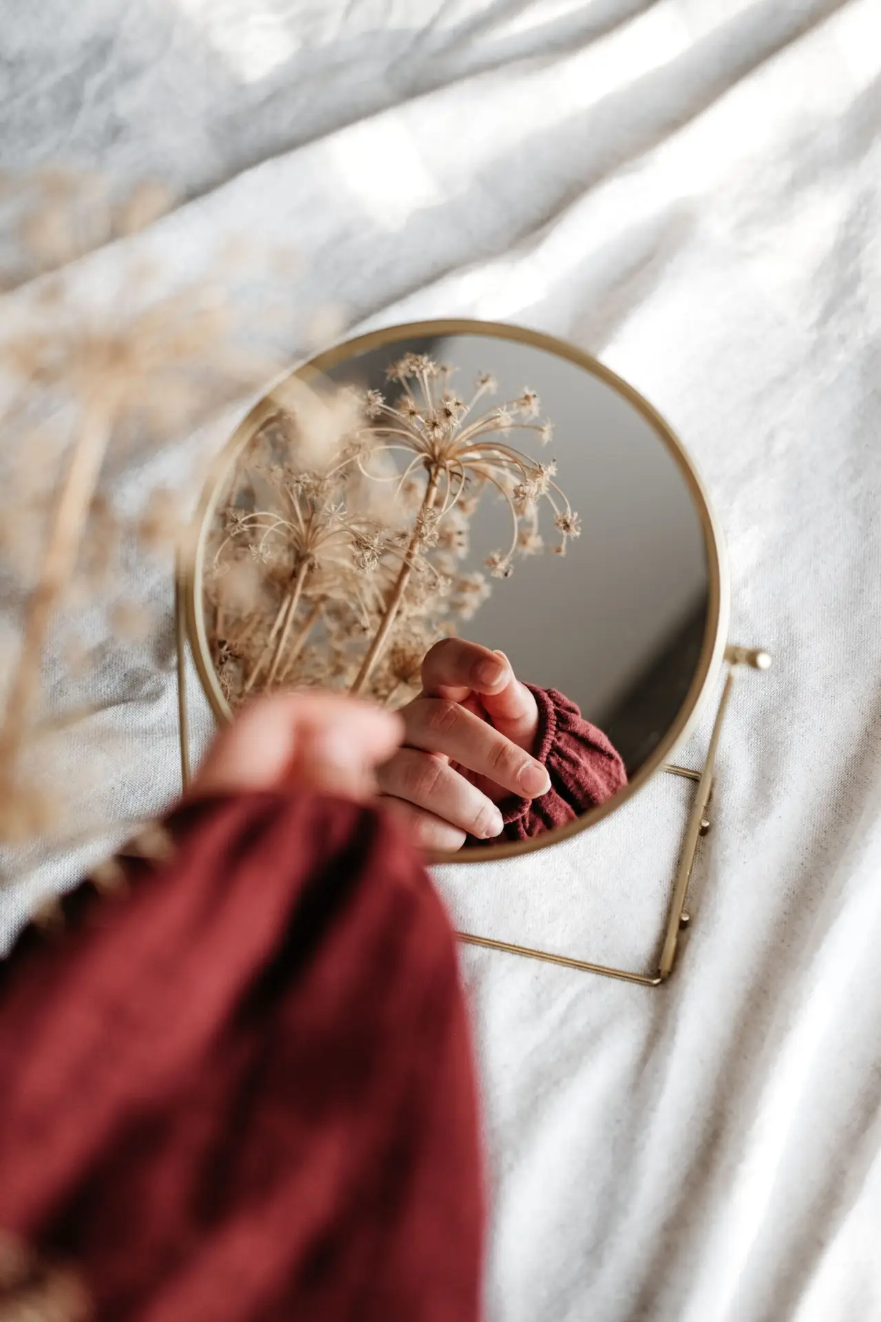 Close-up of a hand holding dried flowers reflected in a round mirror, adding an artistic touch.